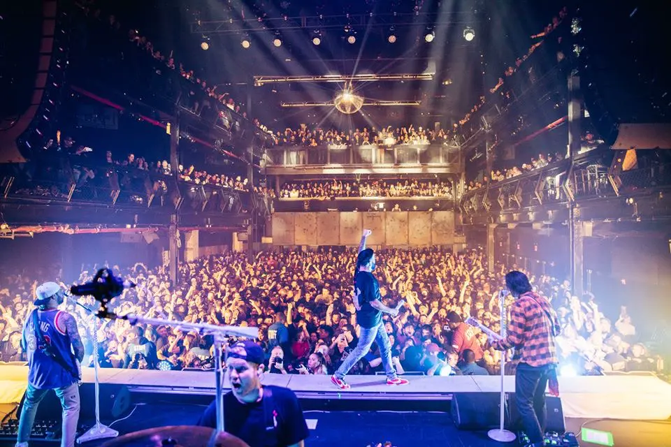 Band on stage seen from behind, facing a full multi-level room
