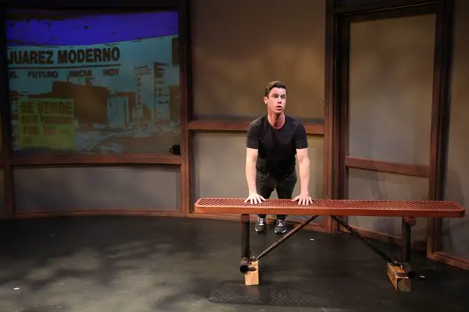 Solo performer at a bench in front of a projection screen